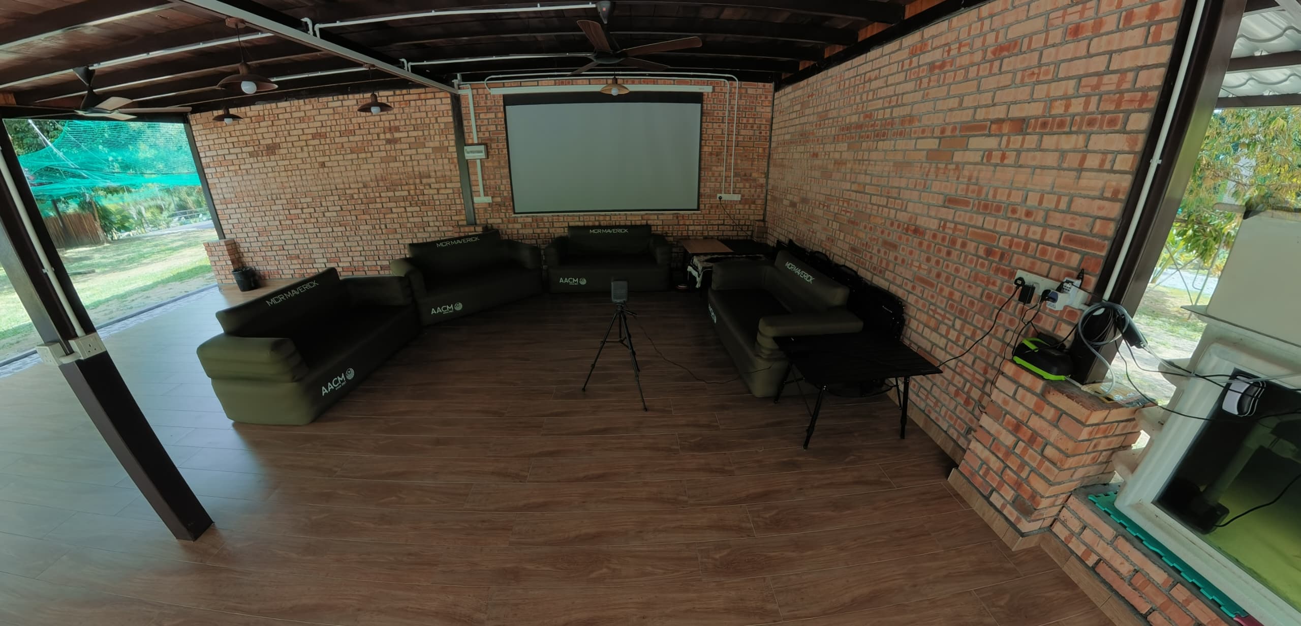 Open-sided hall with brick walls, projector screen and sofas