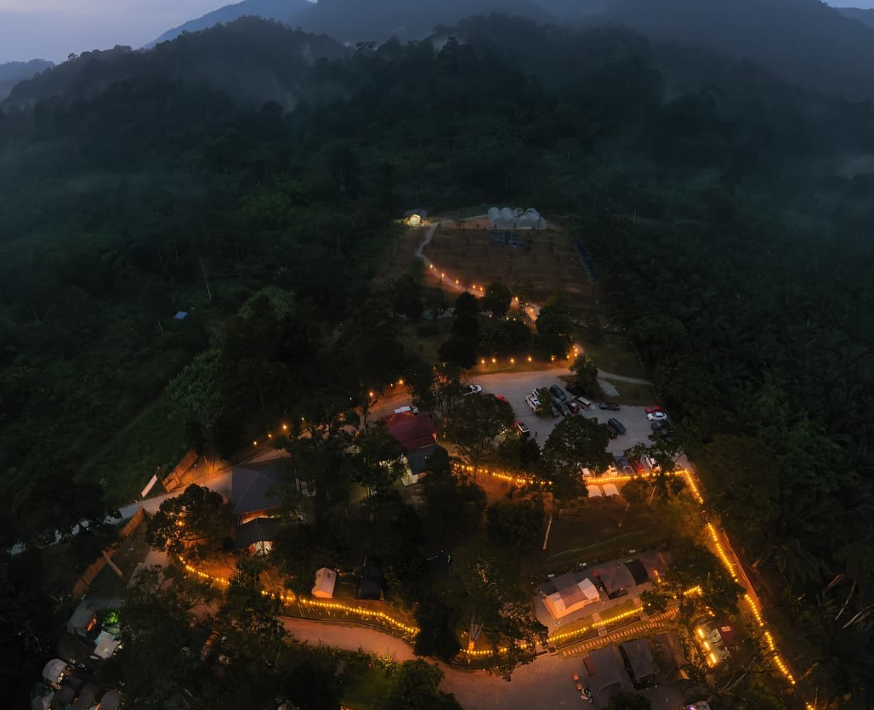 Deru Alam Campsites at dusk, lit by string lights beside the river